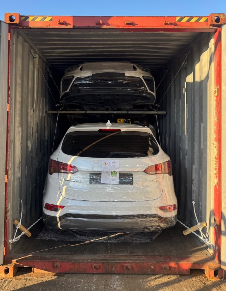 Упакованная задняя часть белого SUV под белым седаном внутри контейнера.