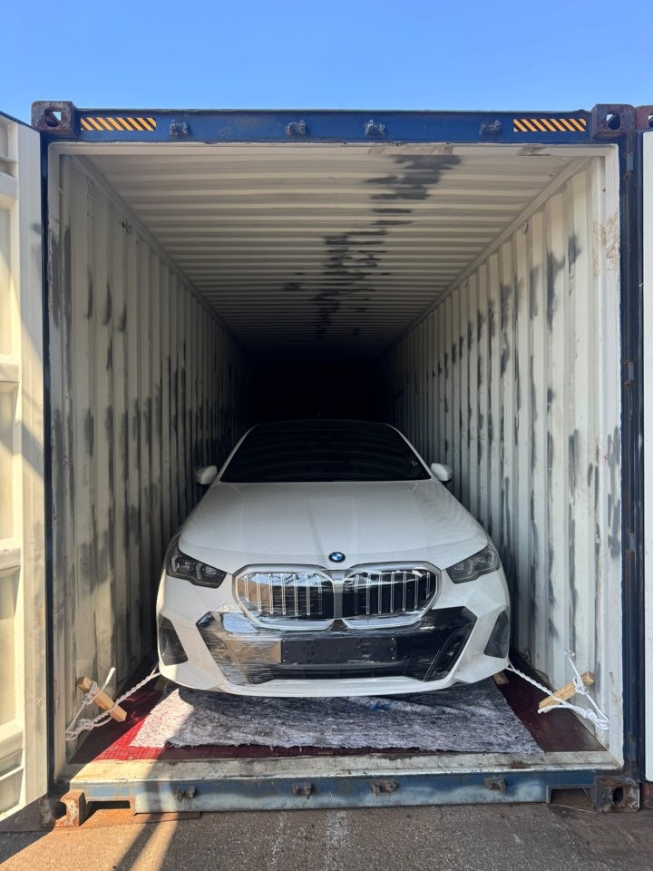 مقدمة سيارة سيدان BMW بيضاء داخل حاوية مفتوحة مع حبال تثبيت على الجانبين.